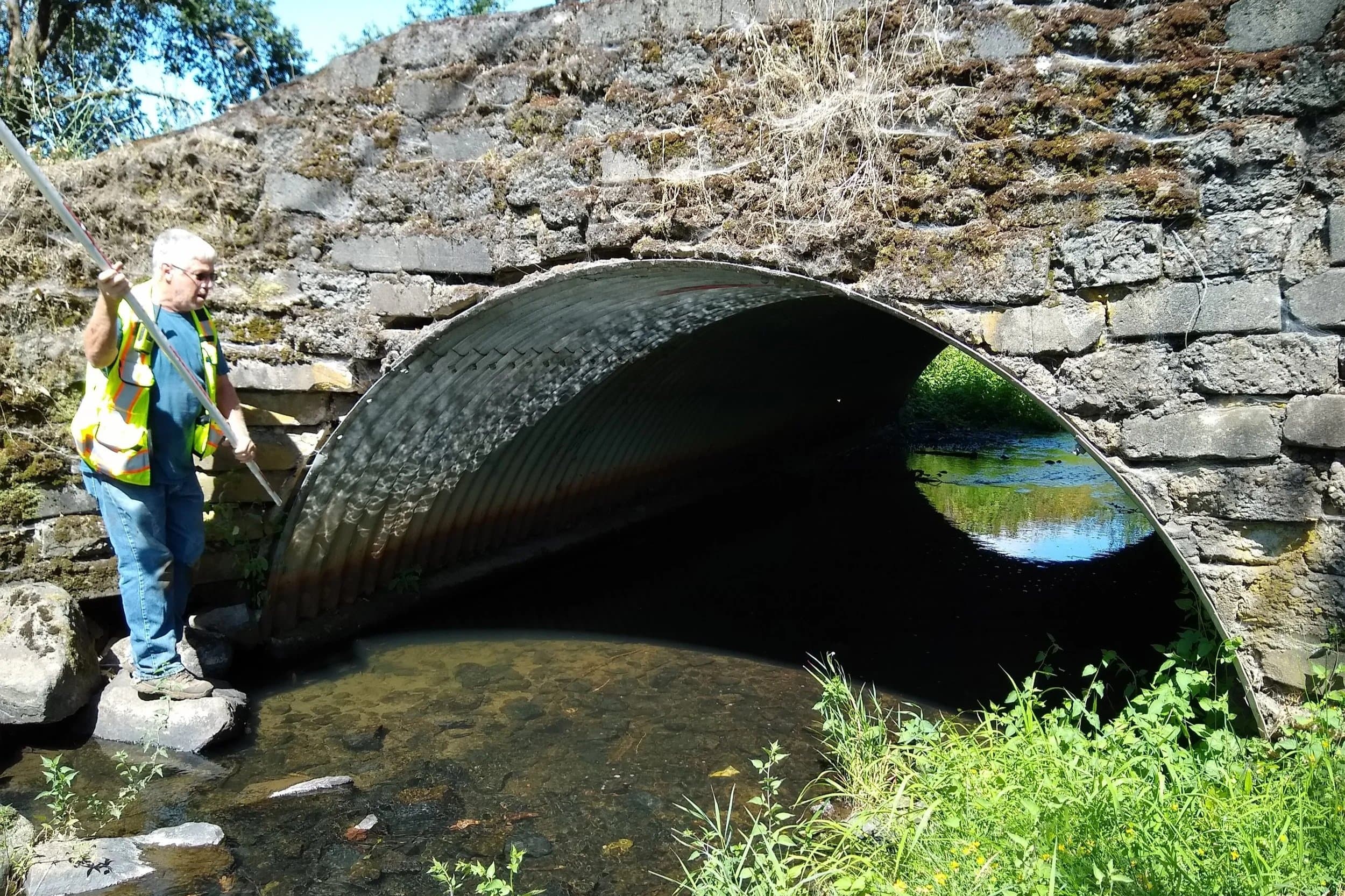 A Boatwright engineer measuring flow at a culvert beneath a historic stone bridge.